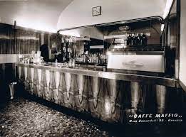 Interno di un bar vintage con un lungo bancone lucido e scaffali dietro barista.